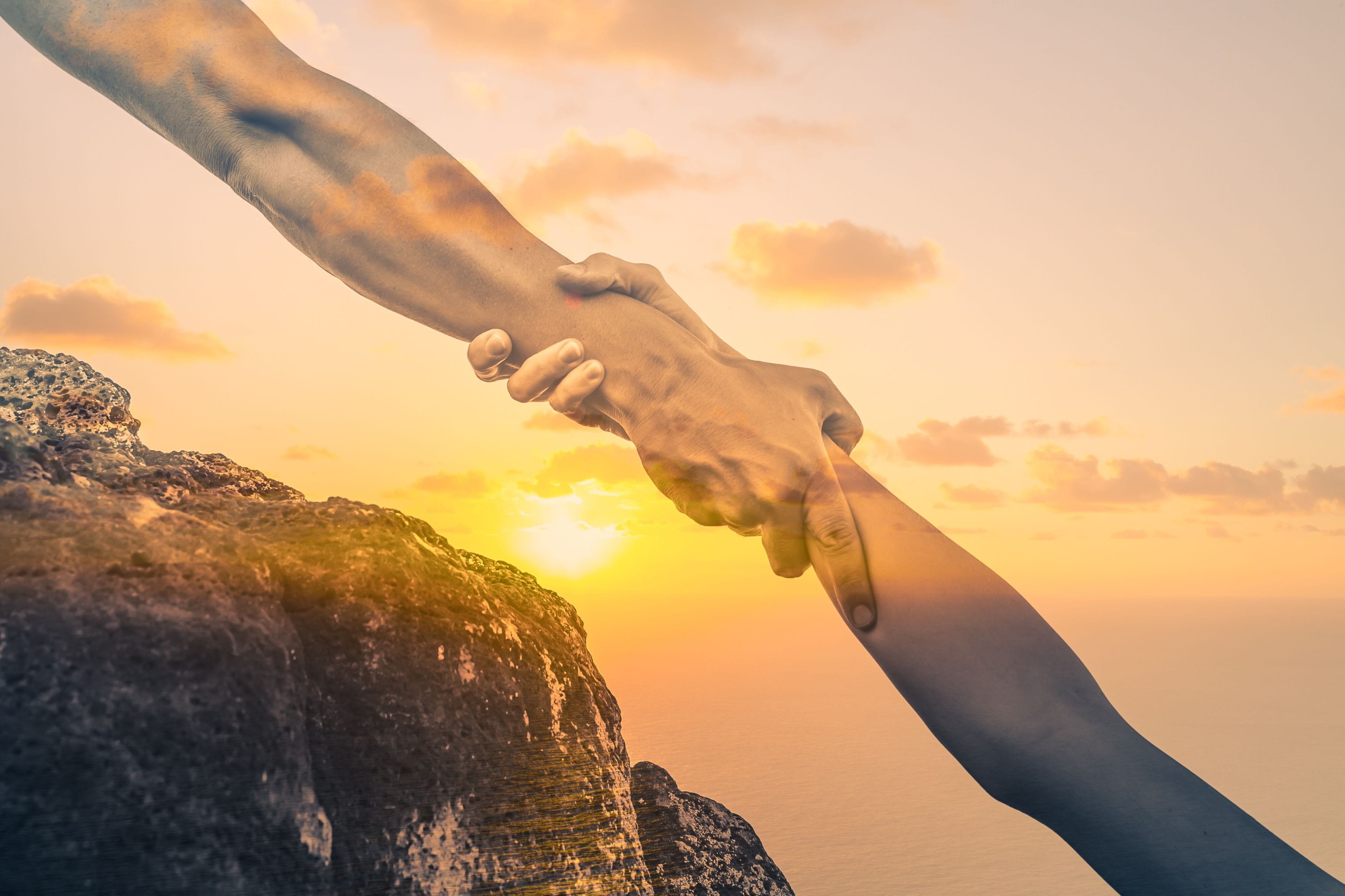 A Couple Of People Holding Hands Over A Cliff